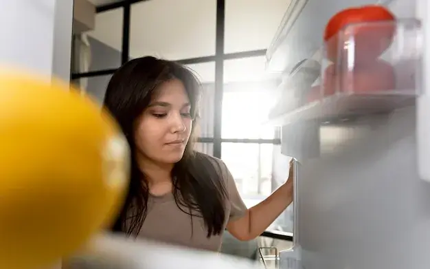 Mulher de pé diante da geladeira aberta, olhando as prateleiras para decidir o que preparar
