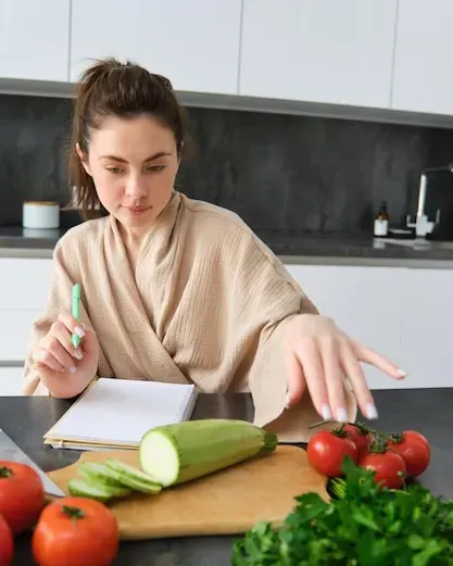 Mulher sentada à mesa da cozinha anotando a lista de compras num caderno