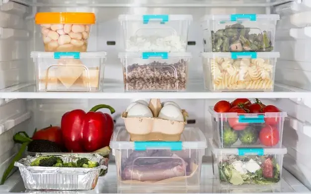 Geladeira aberta com potes de comida guardada e legumes organizados nas prateleiras