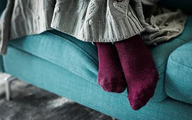 Pés de uma pessoa descansando no sofá da sala, com uma manta amassada ao lado
